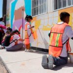 Niños con chalecos fosforecentes pintando un mural